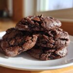 A stack of four fudgy, dark Chocolate Chocolate Chip Cookies piled on a white plate.