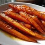 Close-up of glossy Roast Honey Garlic Butter Carrots glistening with glaze and seasoning on a white plate.