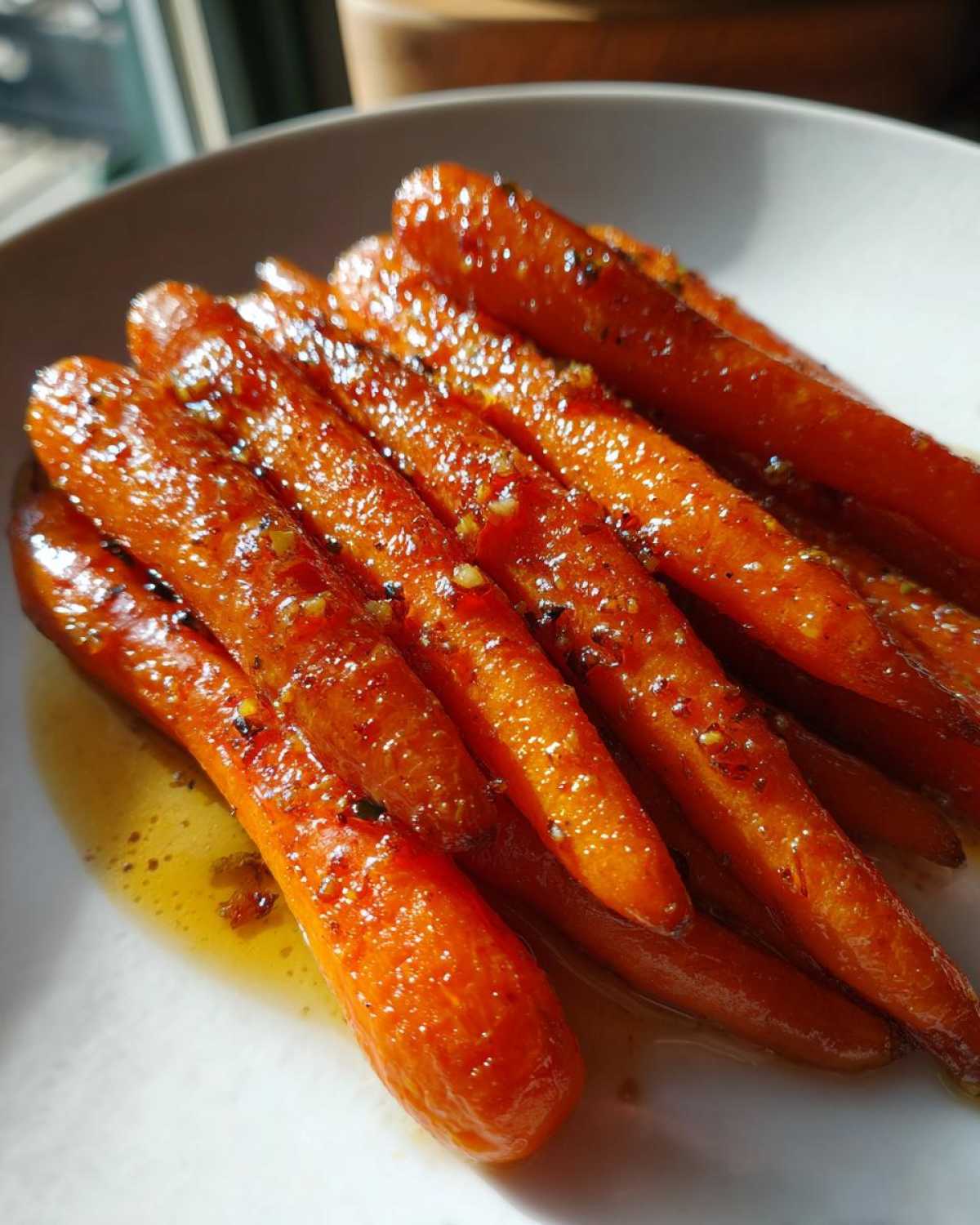 Close-up of glossy, glazed Roast Honey Garlic Butter Carrots resting in a pool of sauce on a white plate.