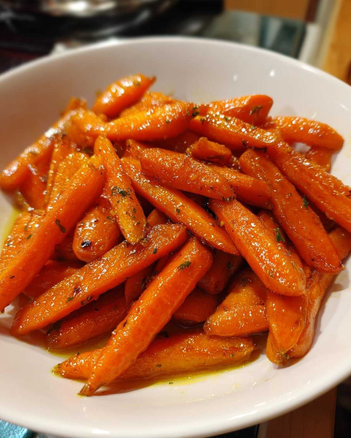 Close-up of tender, glazed Roast Honey Garlic Butter Carrots seasoned with herbs in a white serving bowl.