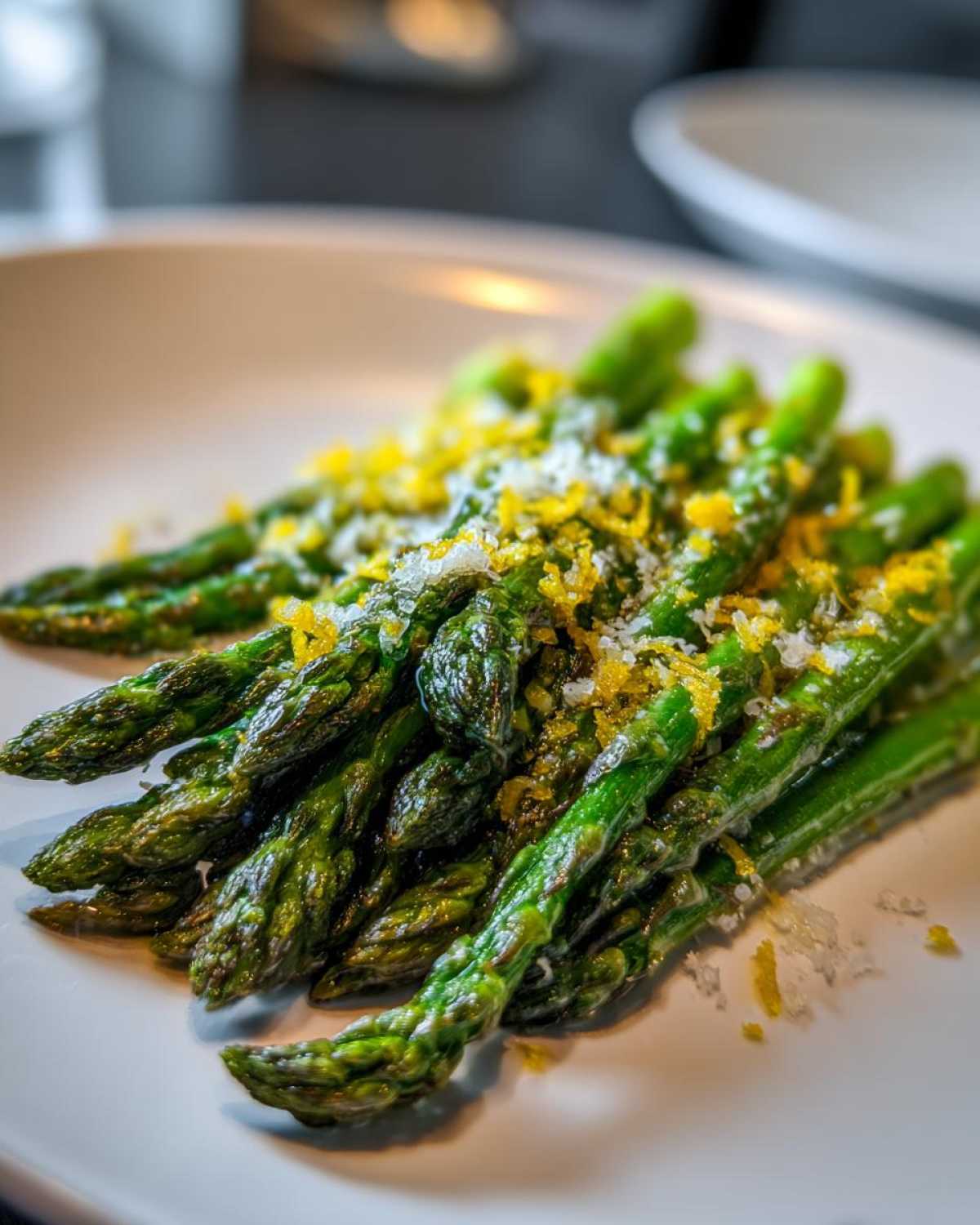 A close-up of perfectly Roasted Asparagus with Lemon and Parmesan, showing bright green spears topped with zest and cheese.