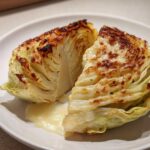Close-up of a roasted cabbage recipe wedge, cut in half, showing caramelized edges and sitting in a pool of creamy sauce.