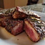 Close-up of medium-rare Roasted Lamb Chops with Garlic Rosemary, showing a beautiful sear and fresh rosemary sprigs.