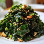 Close-up of a mound of Roasted Peanut Kale Crunch Salad topped with cashews and sesame seeds on a white plate.