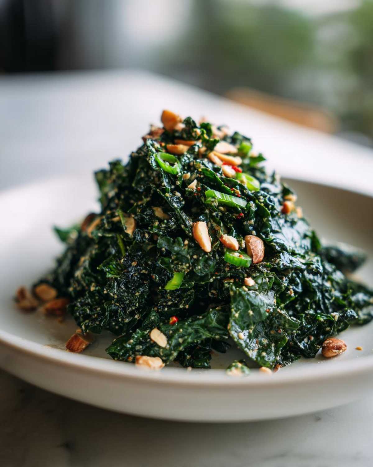 A mound of dark green Roasted Peanut Kale Crunch Salad topped with chopped peanuts and green onions.