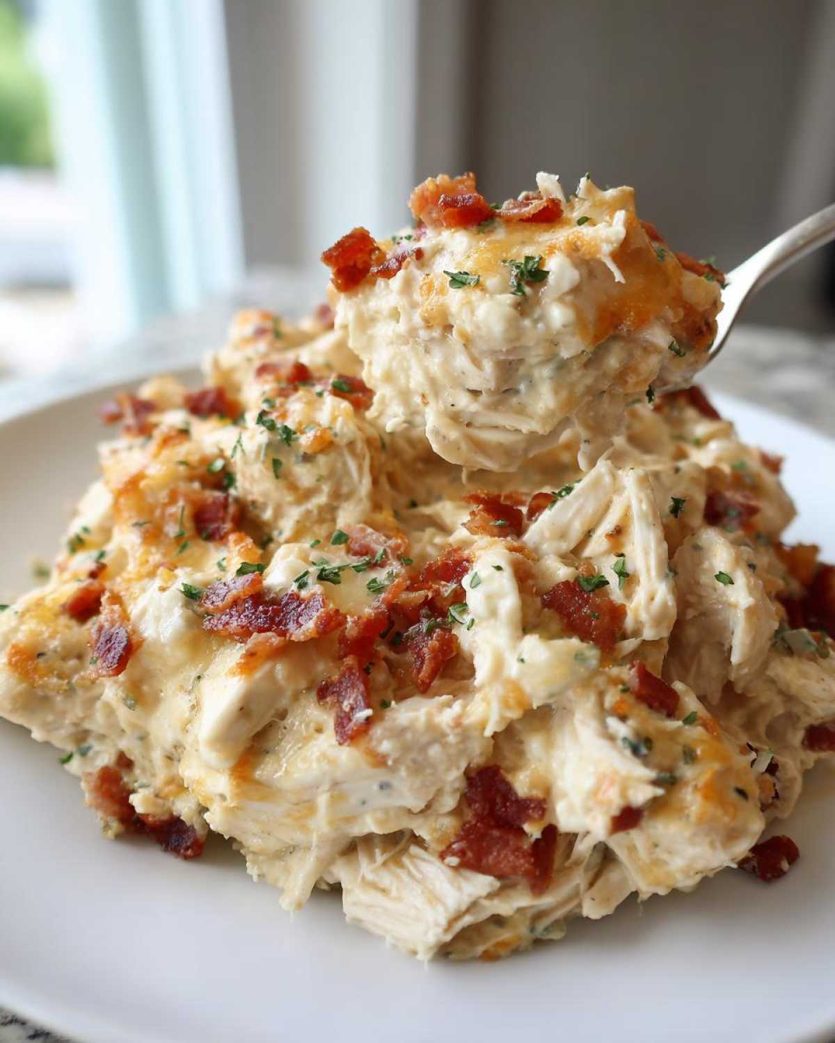 A spoonful of creamy crack chicken casserole topped with melted cheese and crispy bacon bits being lifted from a plate.