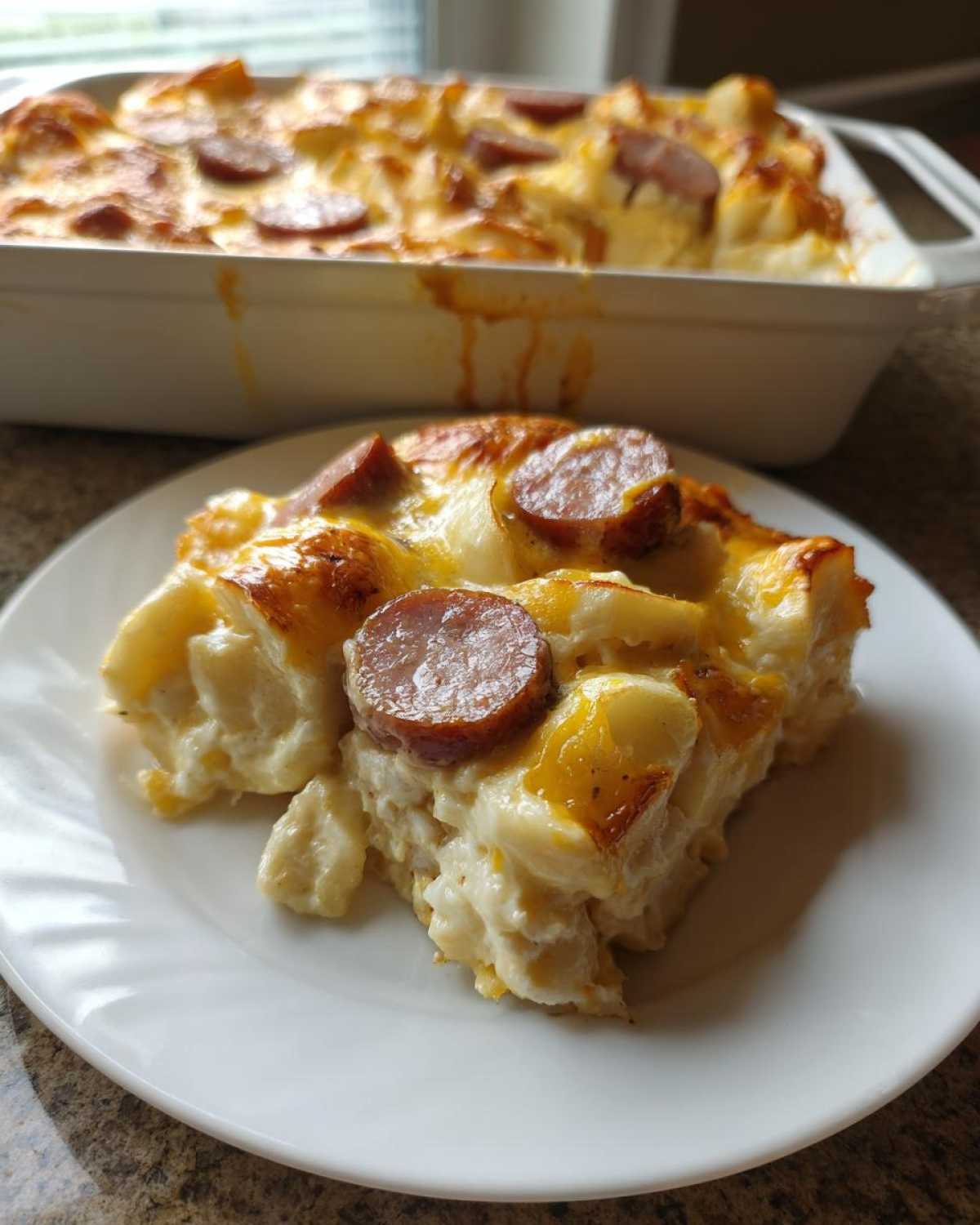 A slice of creamy pierogi casserole topped with melted cheese and sausage rounds, served on a white plate.