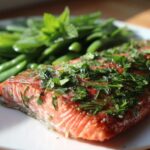 A close-up of perfectly cooked Sheet Pan Salmon with Spring Peas, topped with fresh herbs.