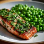 Close-up of a perfectly cooked Sheet Pan Salmon with Spring Peas, topped with fresh herbs.