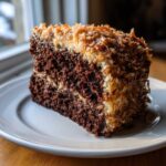 A moist slice of dark chocolate cake layered with filling and topped with toasted coconut, characteristic of german chocolate cake.
