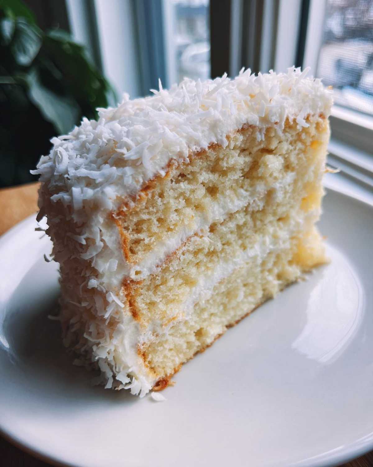 A moist slice of layered coconut cake recipe covered in white frosting and shredded coconut flakes.