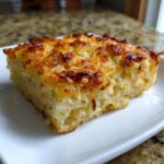 A close-up of a square slice of creamy, cheesy hashbrown casserole with a golden-brown, crispy top.