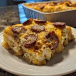 A hearty slice of pierogi casserole topped with melted cheese and sliced smoked sausage on a white plate.