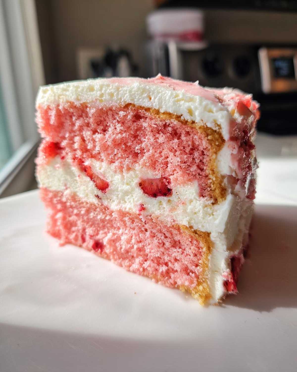 A close-up slice of pink strawberry cake layered with white frosting and fresh strawberry pieces.