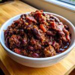Close-up of a white bowl filled with rich, dark Slow Cooker Cowboy Beans featuring kidney beans and chunks of bacon.