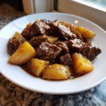 A white bowl filled with chunks of tender Slow Cooker Garlic Butter Beef with Potatoes coated in a rich brown sauce.