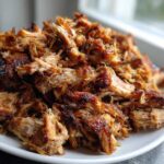 A close-up of perfectly shredded and slightly crispy Slow Cooker Pork Carnitas piled high on a white plate.