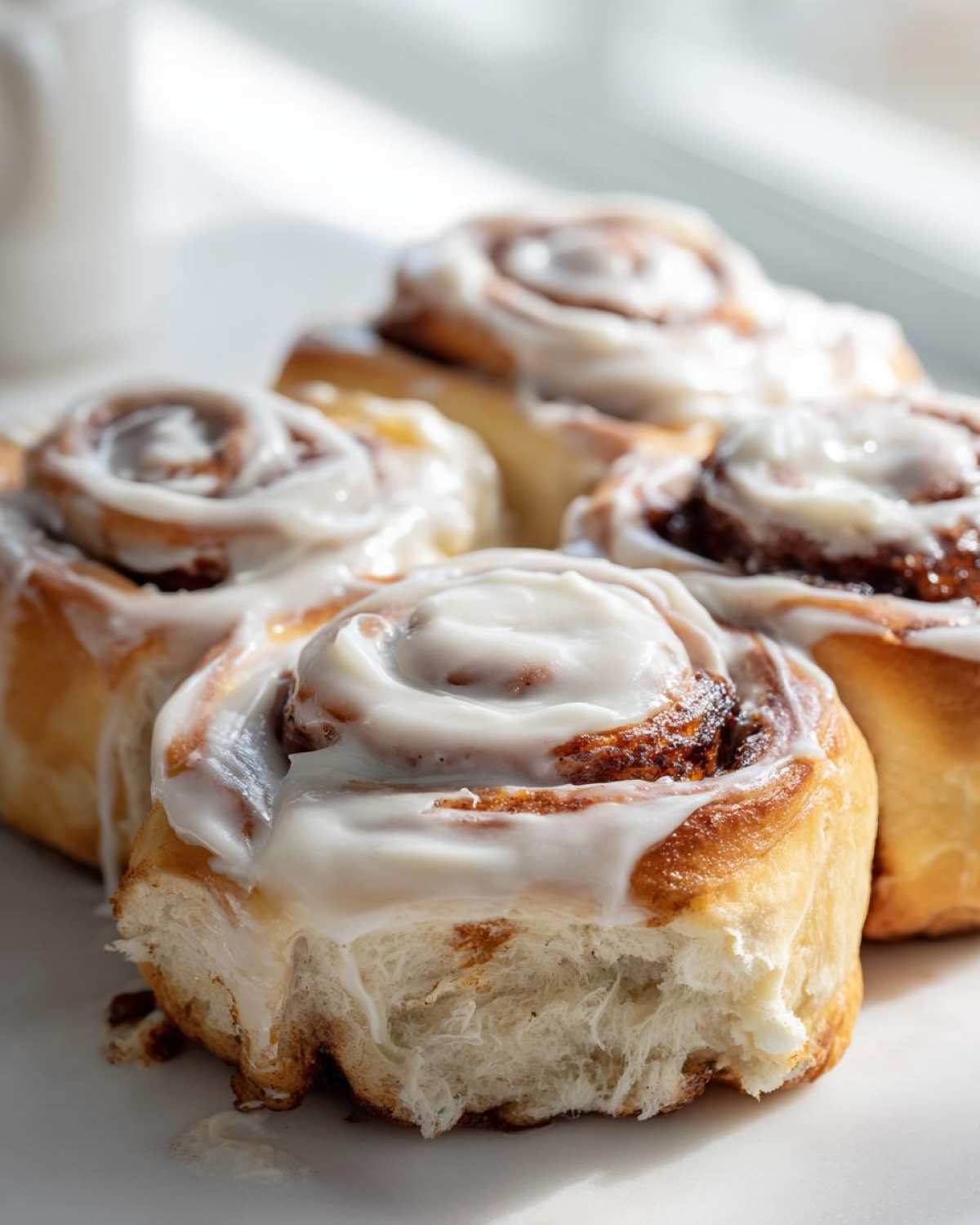 Close-up of several soft cinnamon buns generously topped with white cream cheese frosting, highlighting the fluffy texture.