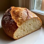 A loaf of freshly baked milk bread, cut in half to show the soft, airy interior and golden, rustic crust.