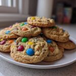 A generous stack of soft, freshly baked m&m cookies piled high on a white plate.