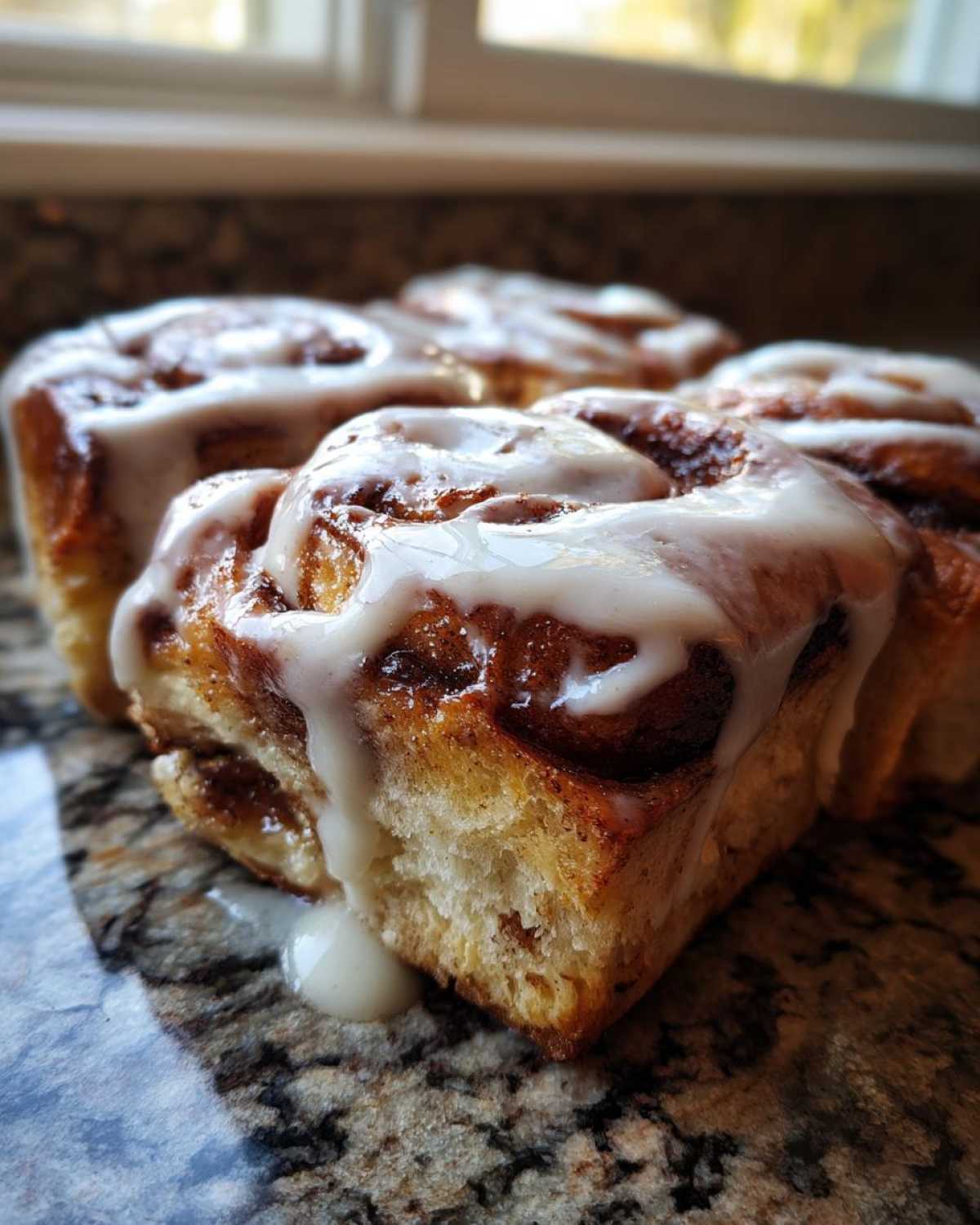A close-up of several freshly baked Sourdough Cardamom Buns drizzled generously with white icing.