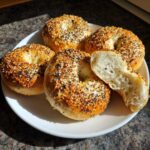 Four golden-brown sourdough discard bagels topped with everything seasoning, one is torn open showing the chewy interior.