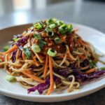Close-up of Spicy Peanut Soba Noodle Salad tossed with shredded carrots and purple cabbage, topped with scallions.