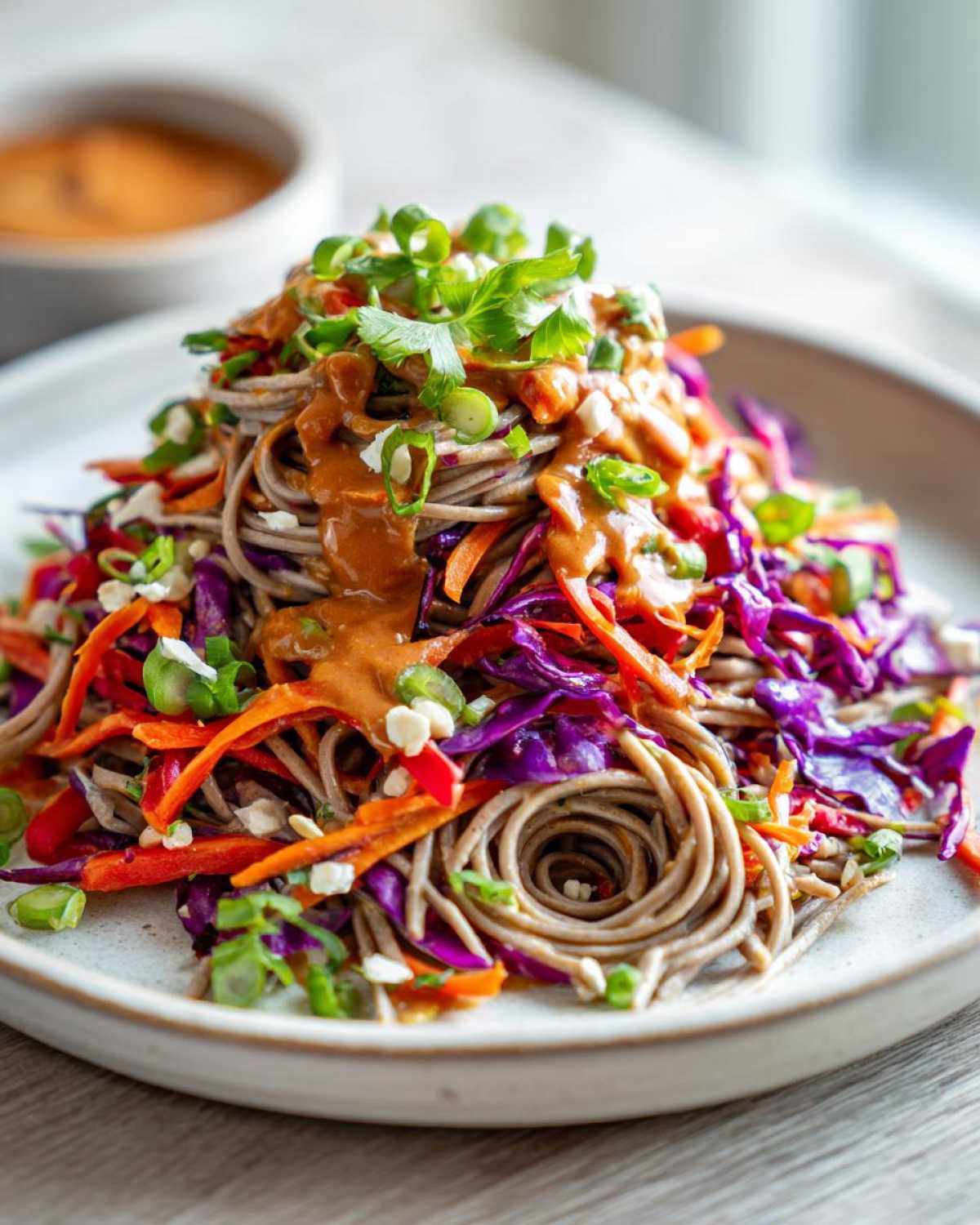 A close-up of a mound of Spicy Peanut Soba Noodle Salad featuring soba noodles, shredded red cabbage, carrots, and peanut sauce.