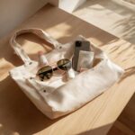 Close-up of essentials in a canvas tote bag, including sunglasses, phone, and beauty products, illustrating what's in your spring bag.