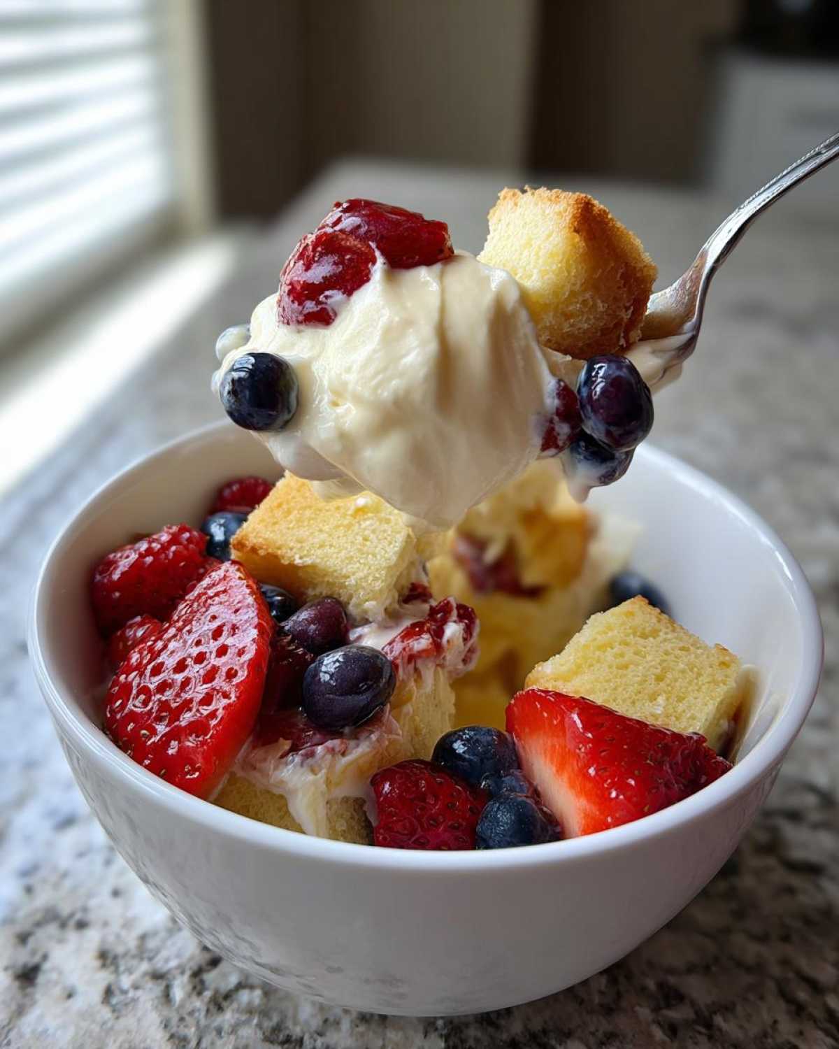A spoonful of creamy custard, cake cubes, and berries being lifted from a bowl of Spring Berry Trifle Dessert.
