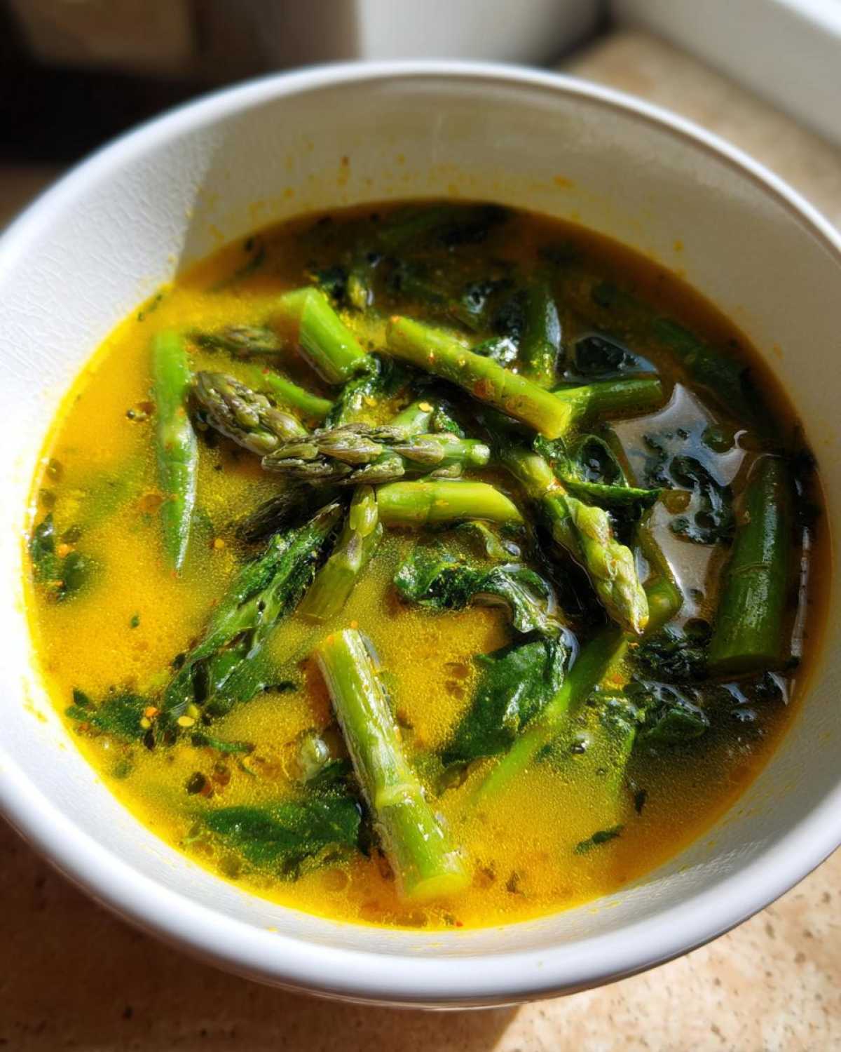 Close-up of a vibrant yellow Spring Detox Soup with Ginger Turmeric featuring bright green asparagus pieces.