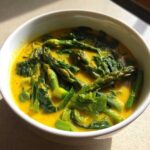 Close-up of vibrant green asparagus and spinach in a rich yellow, turmeric-based broth, part of the Spring Detox Soup with Ginger Turmeric.