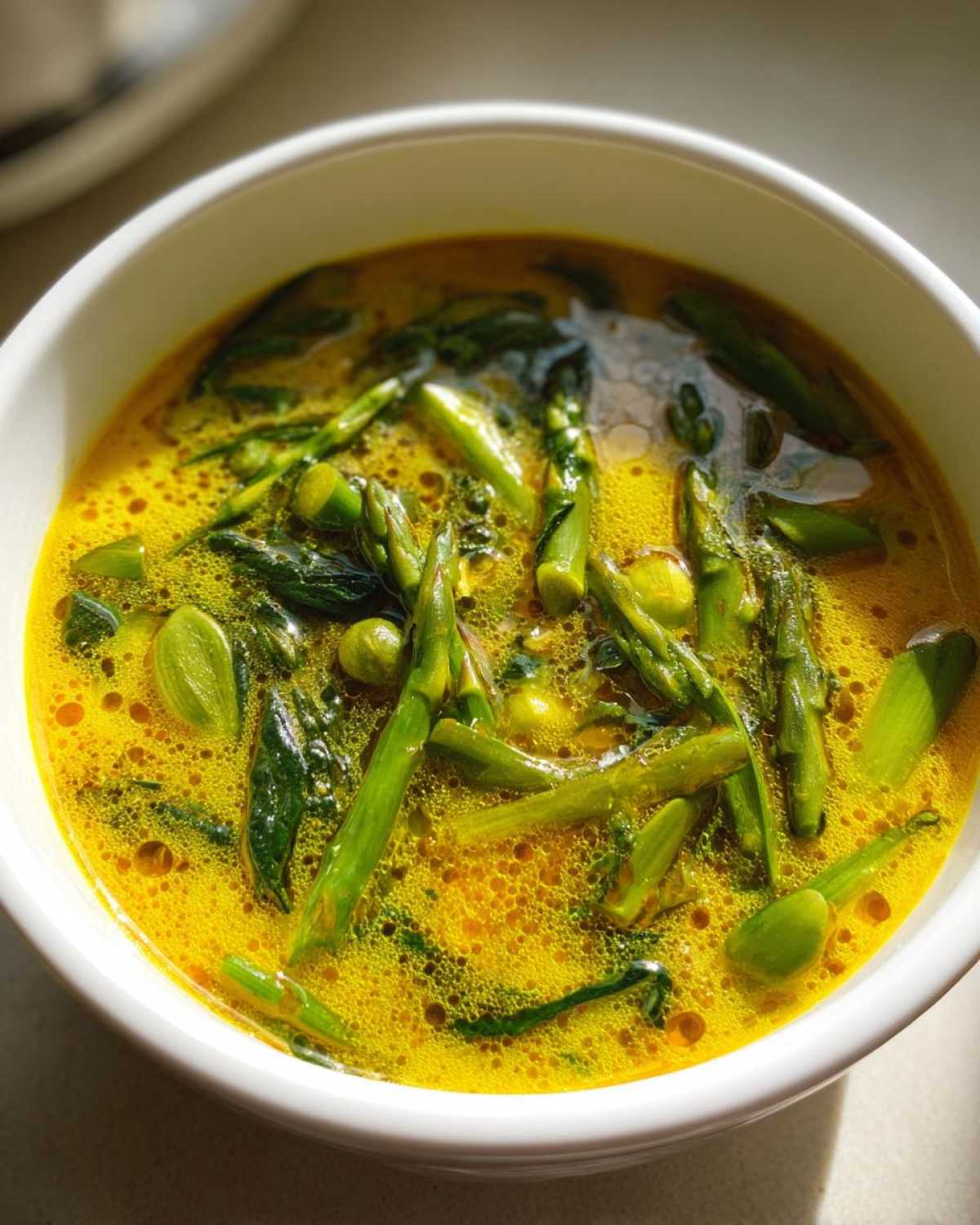 Close-up of a vibrant yellow Spring Detox Soup with Ginger Turmeric, filled with bright green asparagus and spinach.