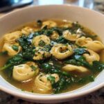 Close-up of a white bowl filled with Spring Soup with Spinach and Tortellini in a savory broth.