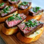 Close-up of perfectly cooked medium-rare steak crostini topped with fresh herbs and garlic.