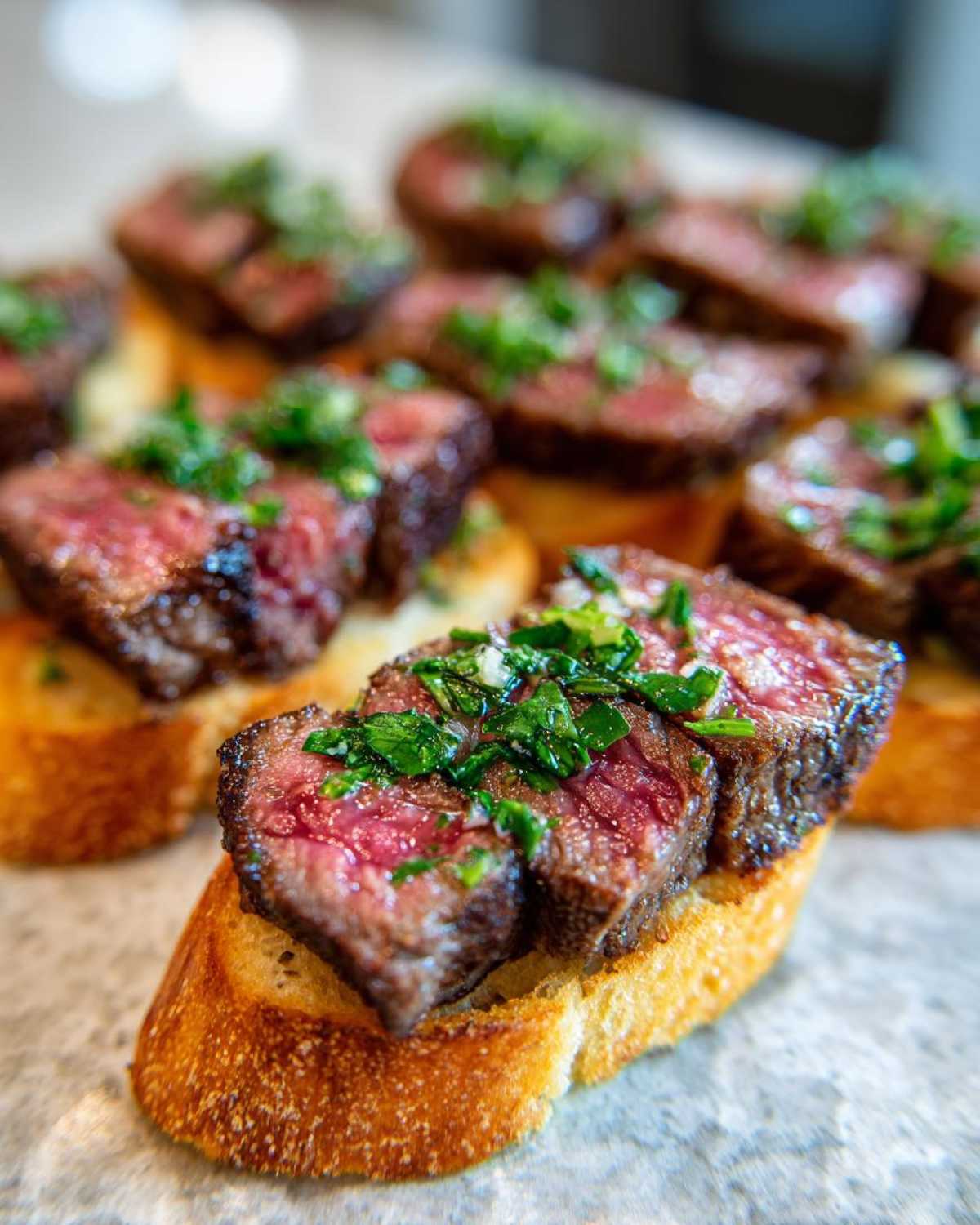 Close-up of perfectly cooked, medium-rare steak crostini topped with fresh green herbs.