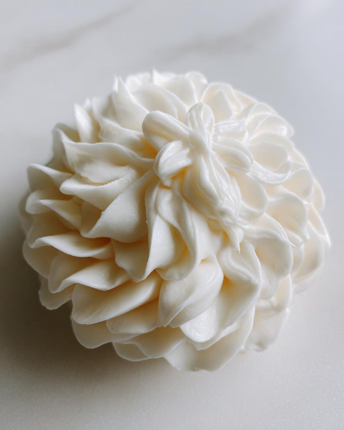 Close-up of stiff, white, piped sugar cookie icing shaped like a ruffled flower bloom.