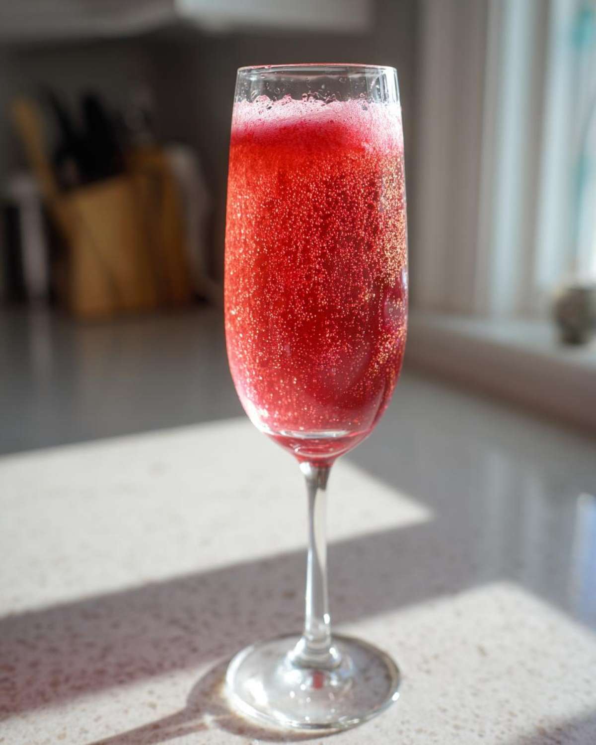 A vibrant, fizzy Strawberry Bellini Brunch Drink served in a tall champagne flute glass on a light countertop.