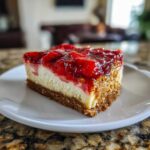 A close-up of a square slice of pretzel salad featuring a thick pretzel crust, creamy filling, and bright strawberry topping.