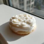 A round sugar cookie topped with thick, white, piped sugar cookie icing shaped like rosettes.