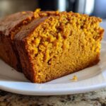 Close-up of two thick slices of moist, orange-colored pumpkin bread resting on a white plate.