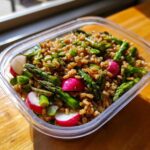 Close-up of a Sustainable Lunch Box Spring Salad featuring grains, bright green asparagus, and sliced pink radishes.