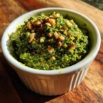 Close-up of bright green Sustainable Pesto with Carrot Tops topped with toasted nuts in a white ramekin.