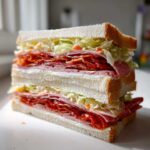 A tall, double-decker Picnic in the Park Sandwiches stacked high with deli meats, lettuce, and white bread.