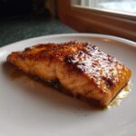 A perfectly cooked fillet of Texas Roadhouse Salmon with a shiny, dark glaze resting on a white plate.