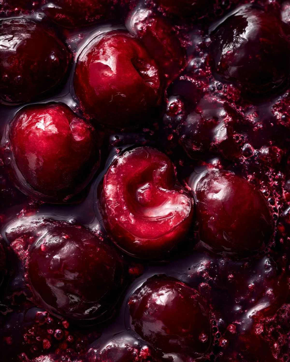 Macro shot showing whole, plump cherries simmering in a thick, dark red liquid, indicative of homemade cherry pie filling.