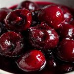 Macro shot of glossy, dark red cherries in thick cherry pie filling, showcasing the rich color and texture.