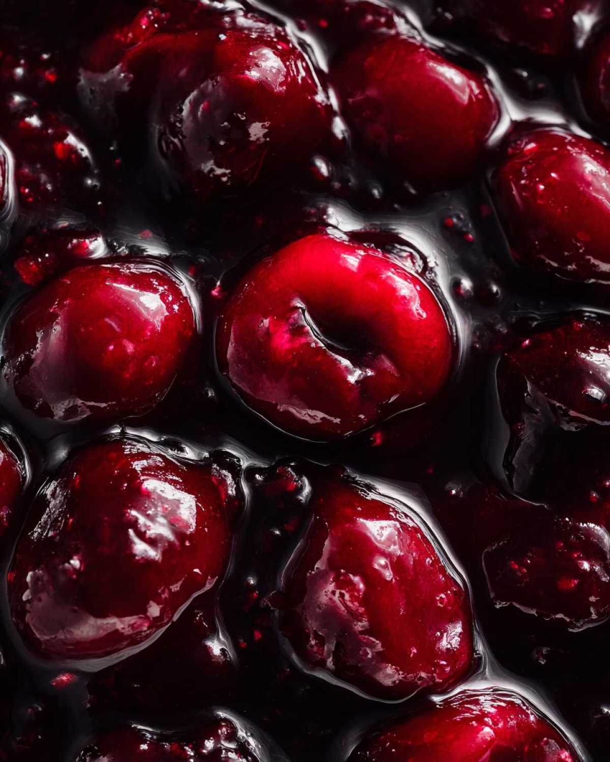 Extreme close-up of glossy, thick cherry pie filling showing whole, dark red cherries suspended in rich, dark syrup.
