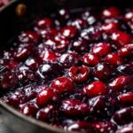 Close-up of glossy, plump cherries simmering in a thick, dark purple sauce, perfect for cherry pie filling.