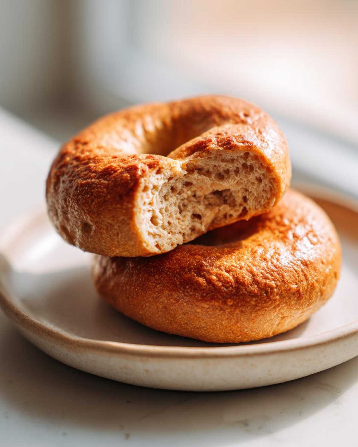 Two golden brown Cottage Cheese Bagels stacked on a plate, with the top one broken open to show the soft interior texture.